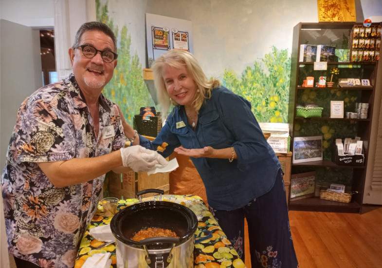 Mark & Laura posing for a picture at a table, sampling food from crockpot.