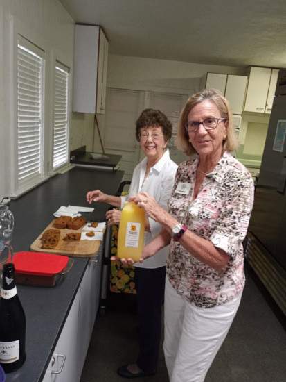 Two women in the kitchen making drinks. One is holding a half gallon of orange juice.